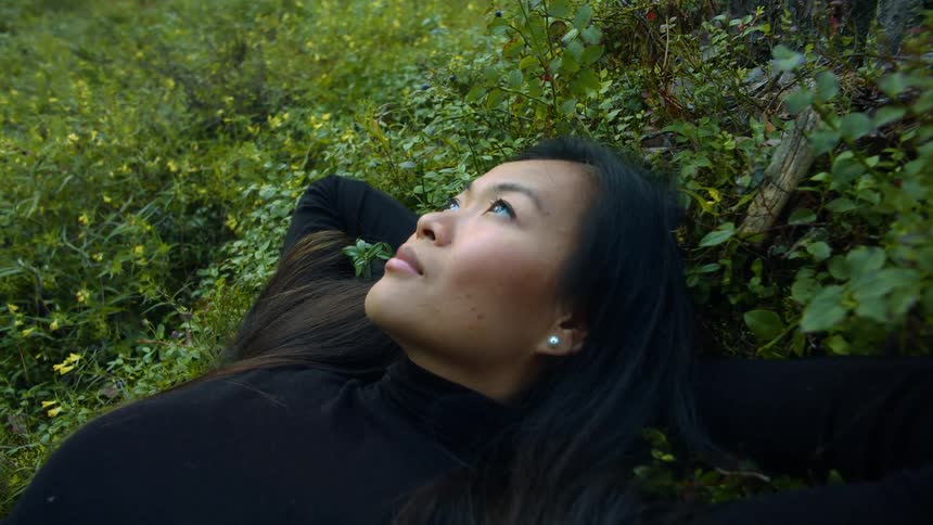 Woman sitting outside in a field of grass staring up at the sky