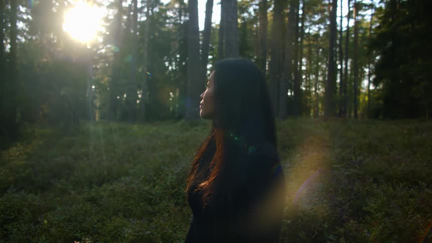 A young woman kneeling on the grass in a forest looks around her and breathes in the fresh air
