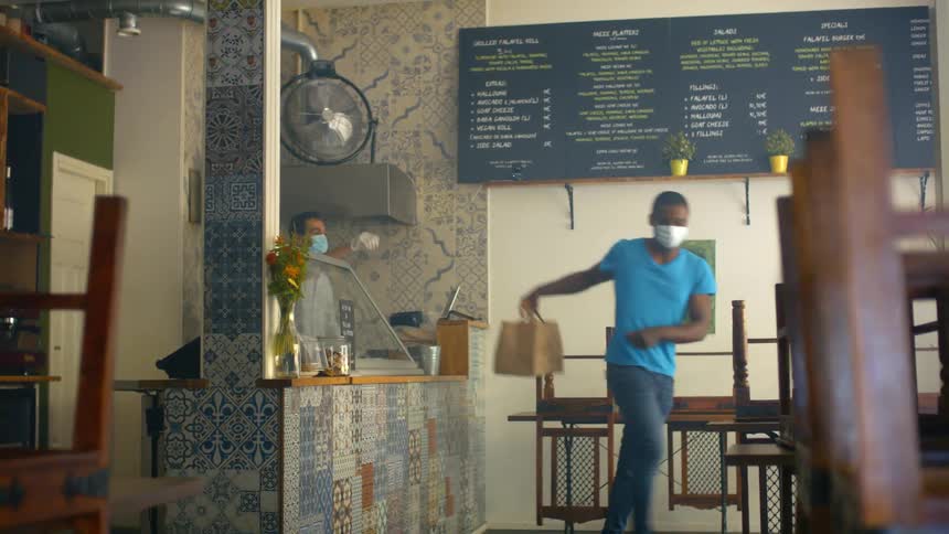 A male customer picks up a food order inside a restaurant from an employee