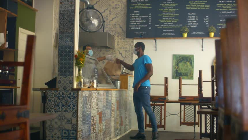 A man walks into a small restaurant and picks up a to go bag from the employee