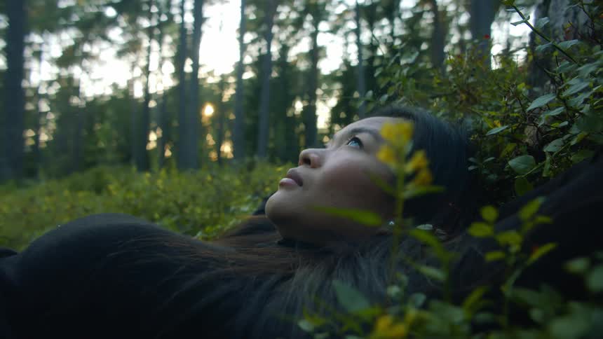 A young woman lies in a field in a forest and looks up to the sky