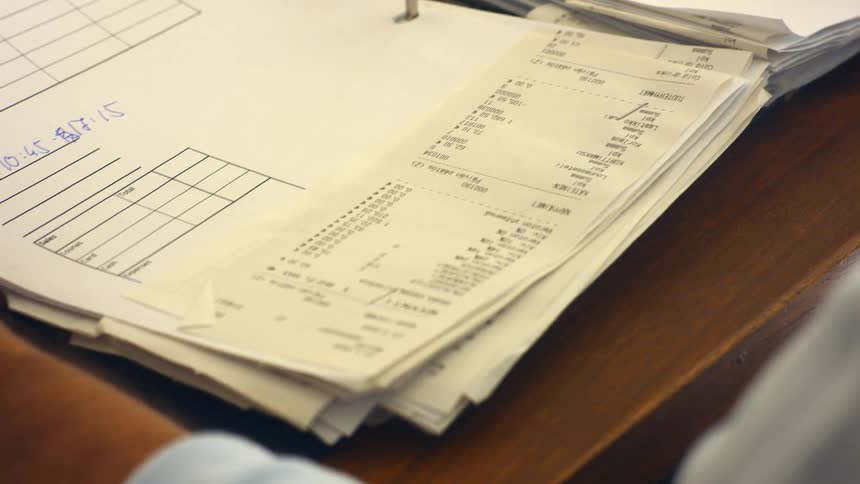 A man sitting at a desk flips through a binder filled with papers and receipts