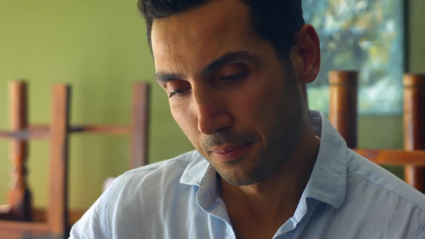 A man is sitting indoors looking down at something in front of him
