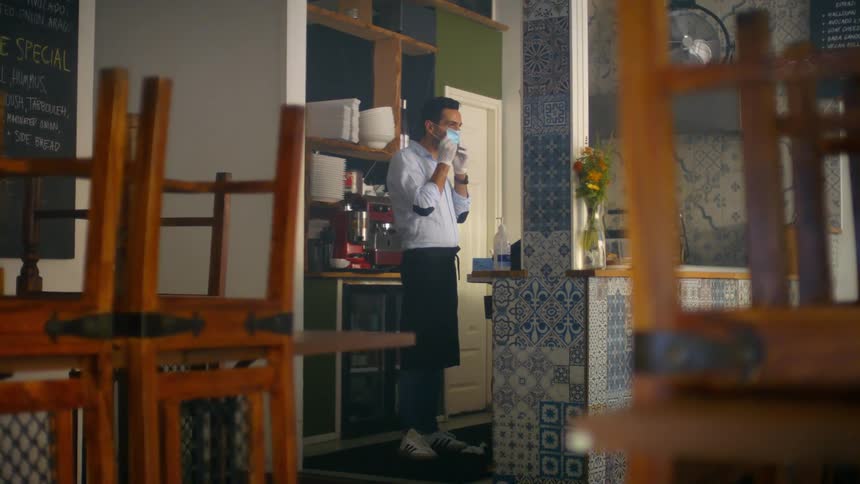 A restaurant employee stands behind the main counter and puts a face mask on