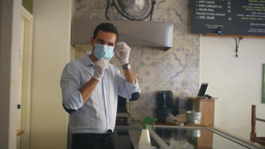 A man standing in the kitchen of a closed restaurant puts a medical mask on his face