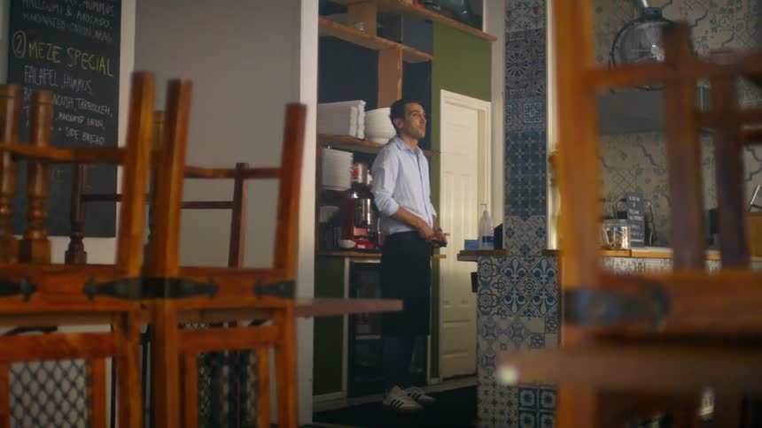 A man ties an apron around his waist as he stands in the kitchen of a close restaurant