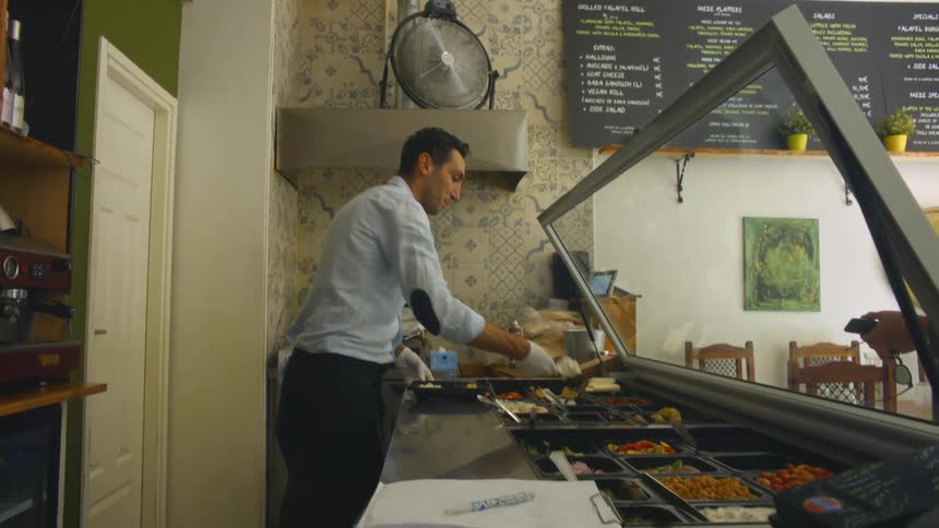 A man scoops food onto a tray for a customer in a small restaurant during the day