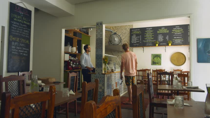 A man standing in a restaurant and pointing out a sign for the man behind the counter