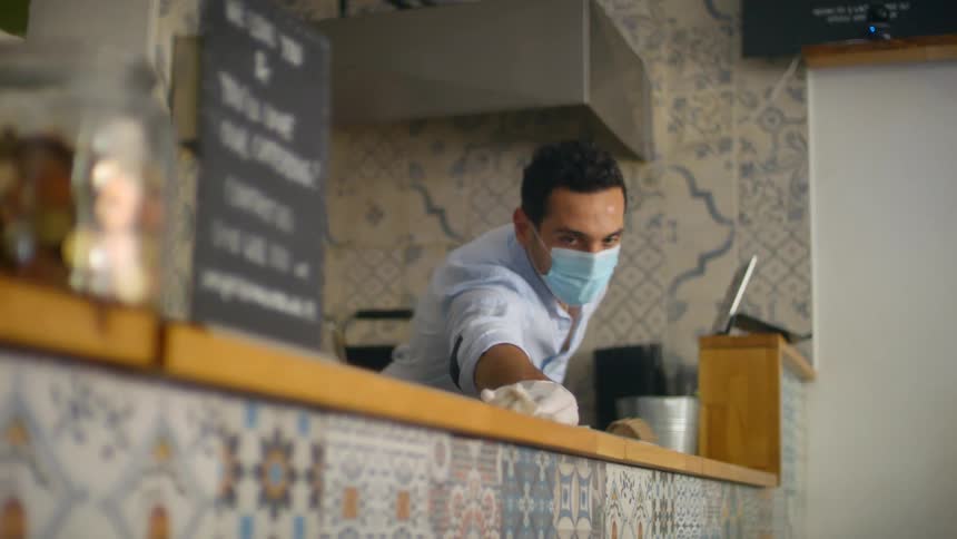 Man wearing a facemask cleaning a checkout counter in a restaurant