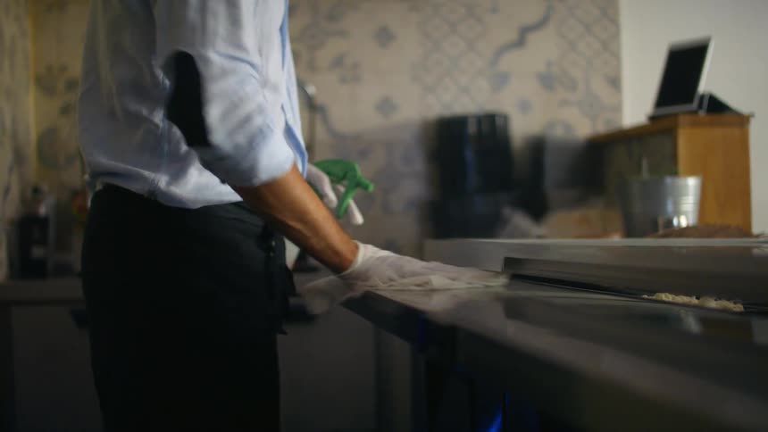 Man wearing disposable gloves spraying and wiping down a counter top