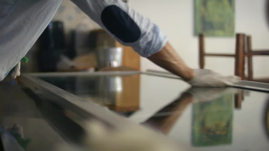 A person clean a piece of framed glass on a table with a towel inside