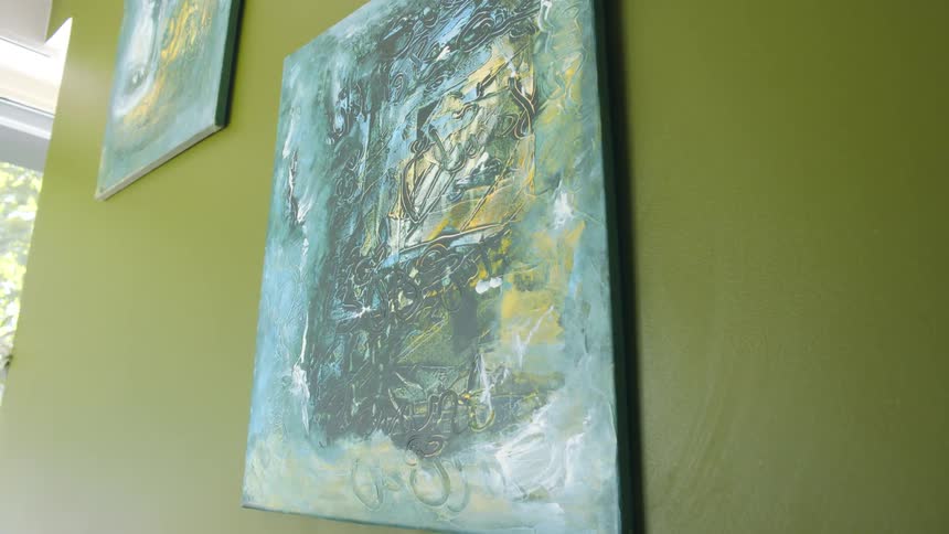 An oil painting of green blue and yellow hangs on a green wall inside