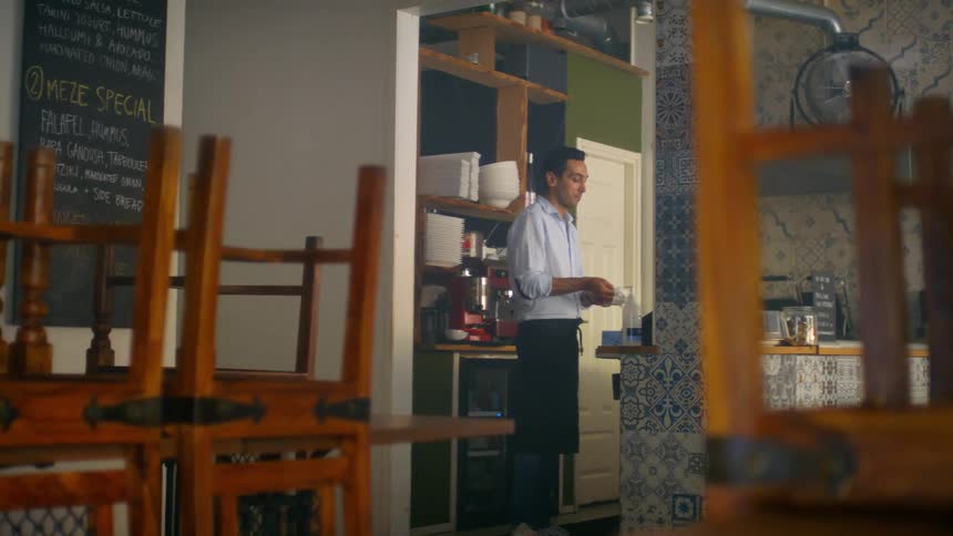 A man standing in the kitchen of a closed restaurant disinfects his hands before putting on a pair of plastic gloves