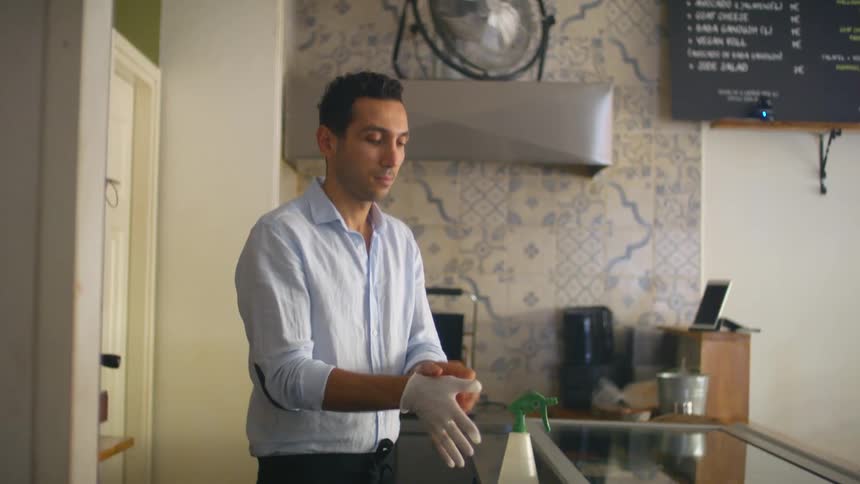 Man standing behind a cafe counter putting on a pair of gloves