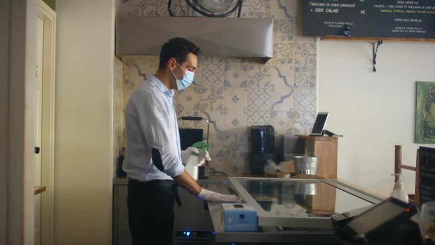 A male employee puts a face mask on and cleans a glass counter