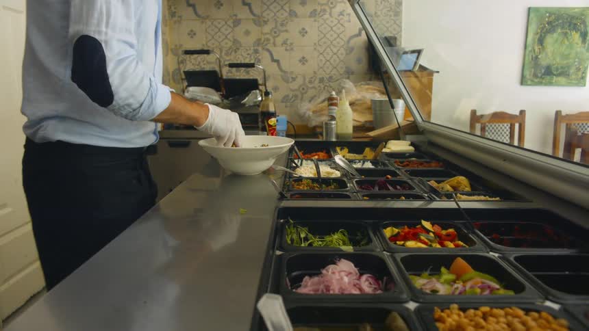 A person with a wristwatch and gloves putting vegetables in a bowl