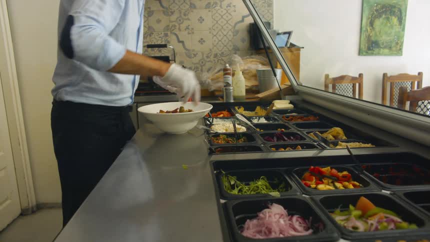 Man preparing food in a bowl behind a counter at a food bar