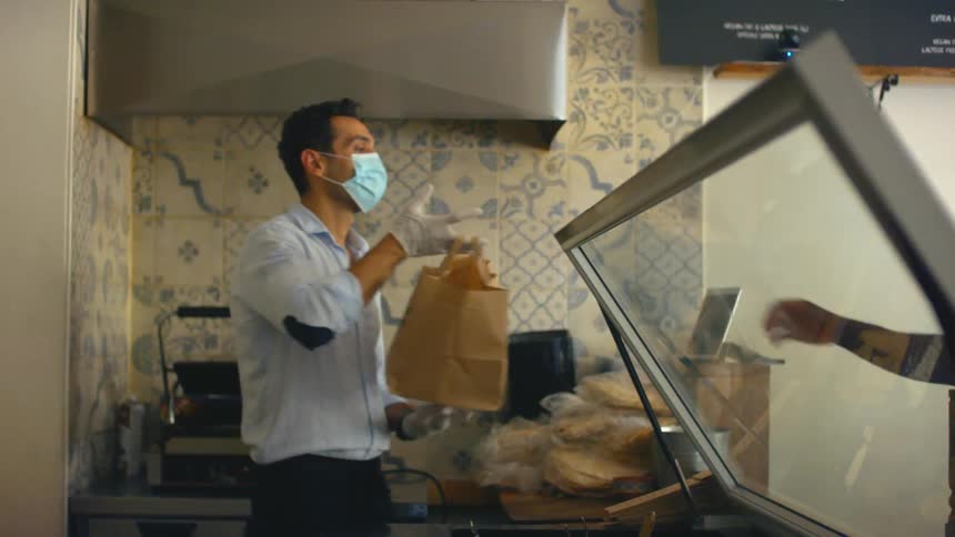 Restaurant worker passing food to a customer from behind a counter