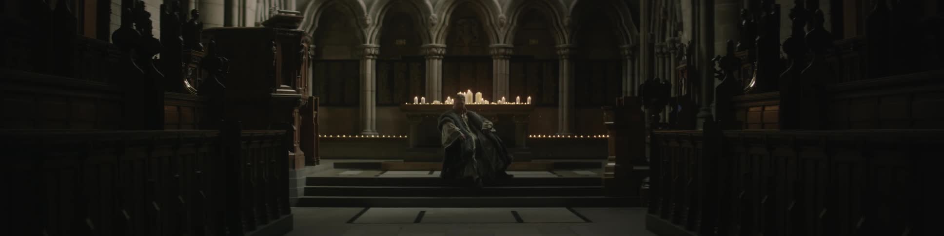 A priest sitting in front of a candle-laden alter
