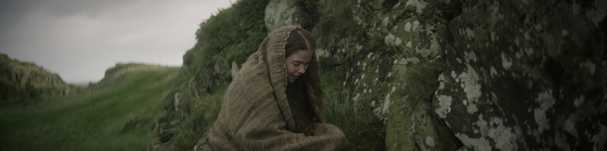 A woman is crawling along a rock filled hill while crying