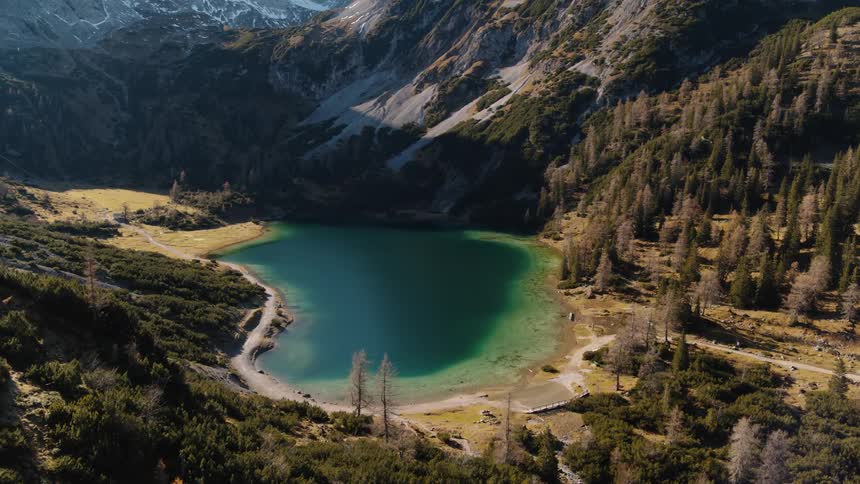 A lake is tucked away at the base of snow covered mountains and surrounded by forest
