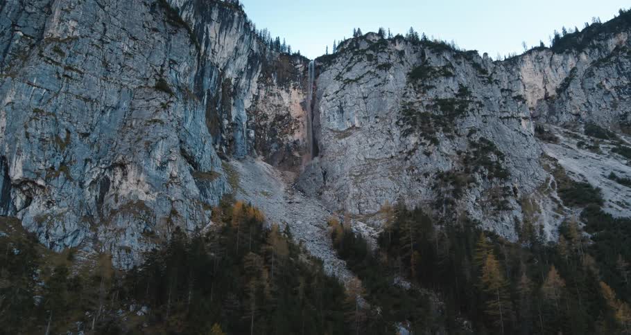 A forest with trees with a cliff and waterfall the sky and clouds in the background