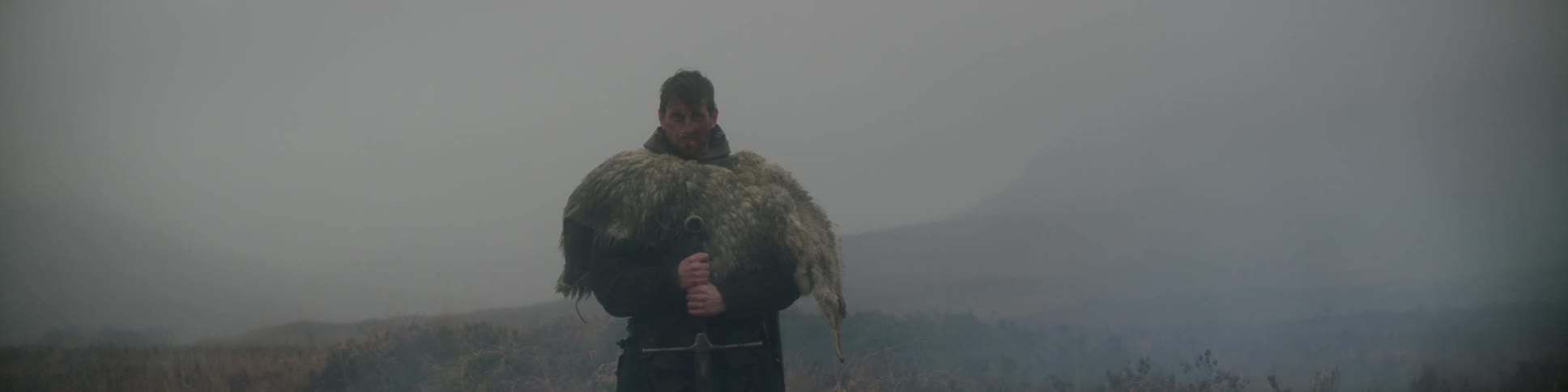 A medieval man holding a sword as he stands in a foggy field