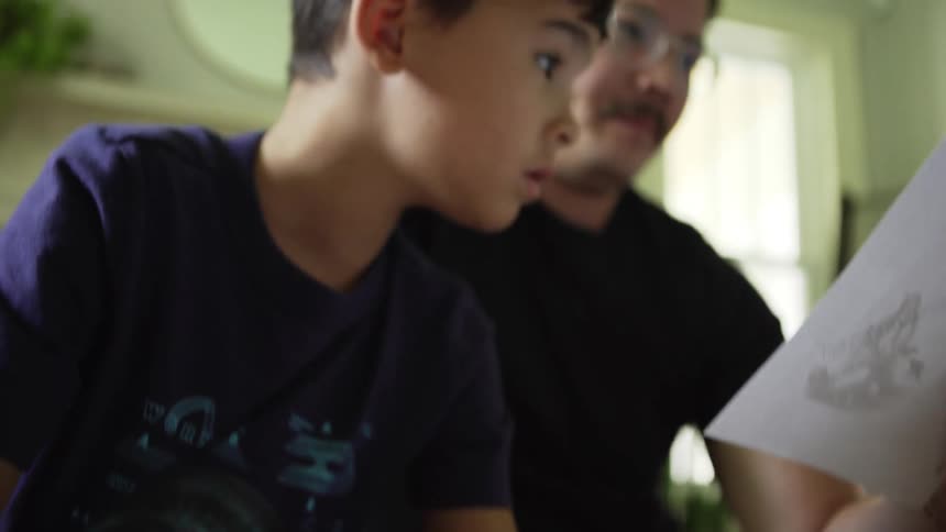 Father with a mustache and son look at a paper and use a tablet in the living room at home