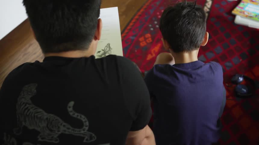 Father and son sitting on a rug in a room reviewing homework
