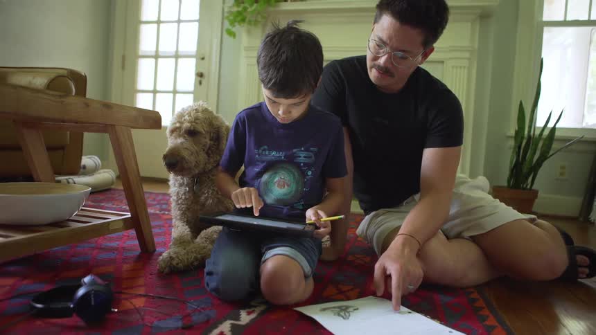 Boy sitting in living room with father working on a tablet and school work