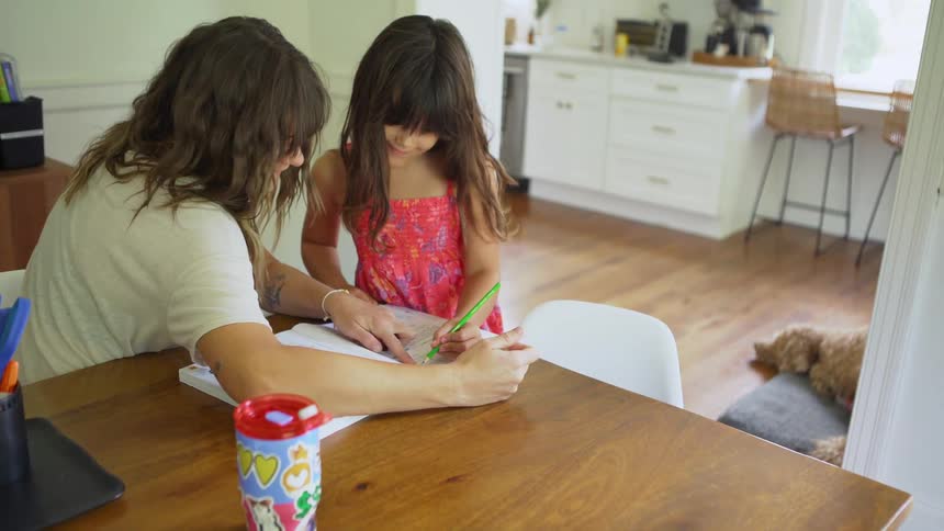 Mother and daughter sitting at a table in their dining room working on the little girls homework in a textbook