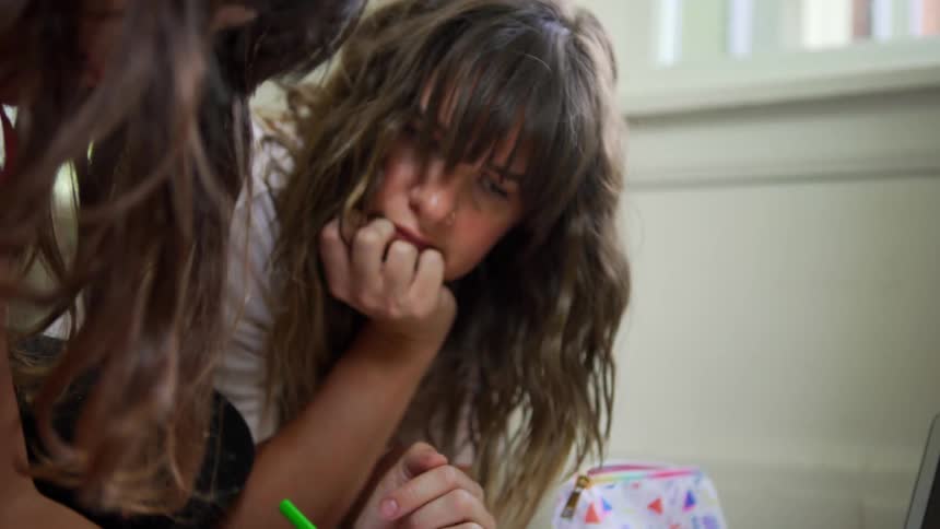 Two girls sitting on the floor in a room working problems in a textbook