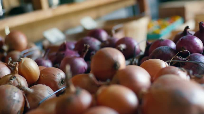 Yellow and red onions sit in wire bins in a market