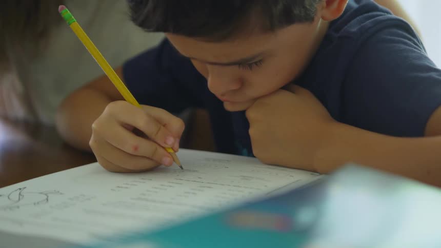 A boy is deep in thought as his mother helps him with homework