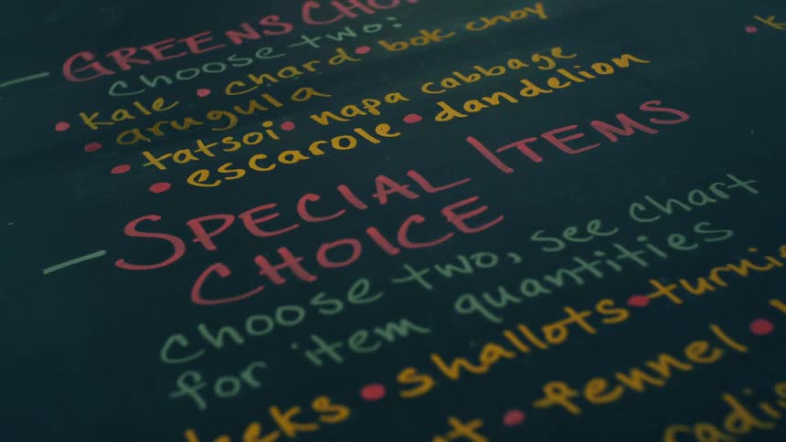 Writing on a black board sign in different colors tells the specials of a restaurant