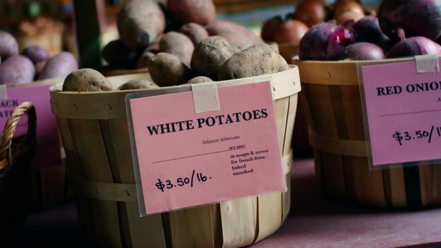 Potatoes and onions in open baskets labeled with handwritten prices