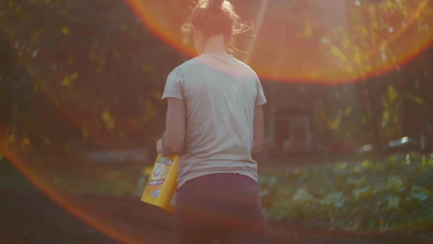 A young woman walks through a field while sowing seeds on a sunny day