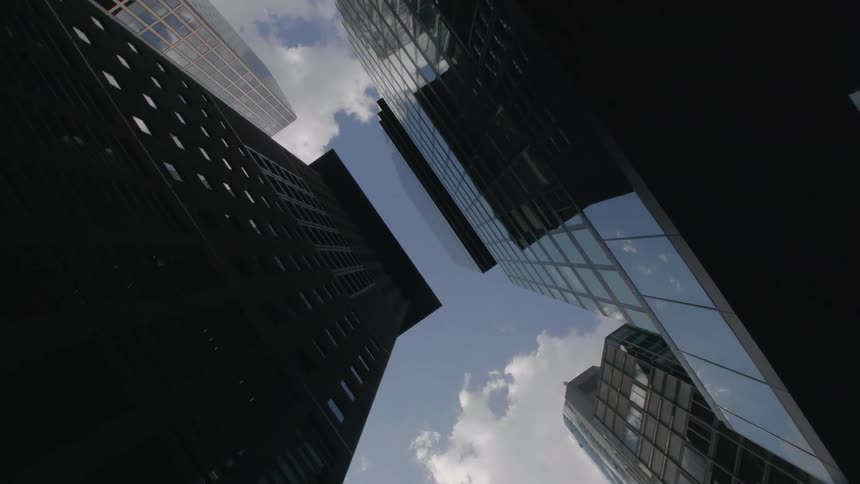Tall buildings along a downtown street in midday reflecting the sky and clouds