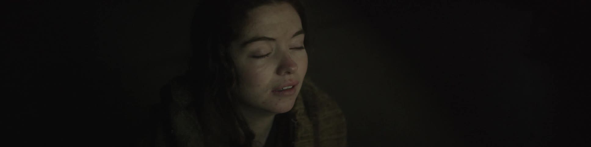 A woman sitting in the dark closes her eyes