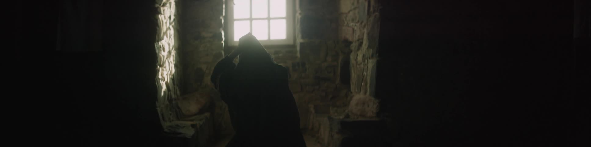 A woman standing in front of a window pulls a hood up over her head