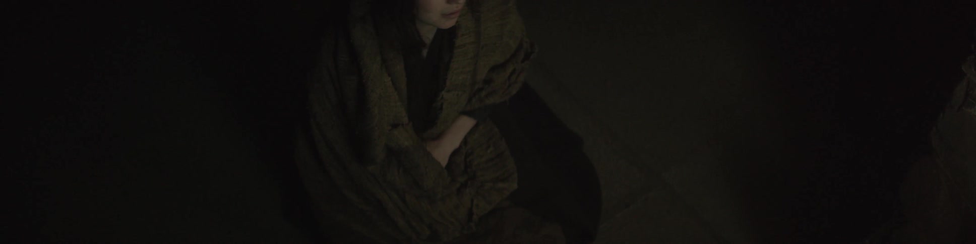 A woman is sitting down in a dark area with her eyes closed