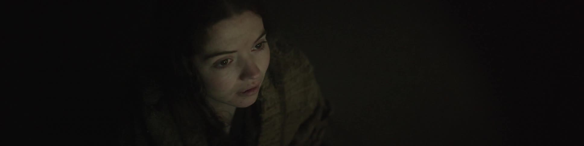 A woman is staring forward in a dark area