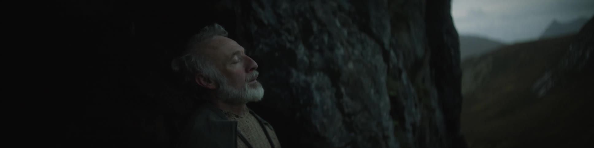 An elderly man resting his head against a cave wall