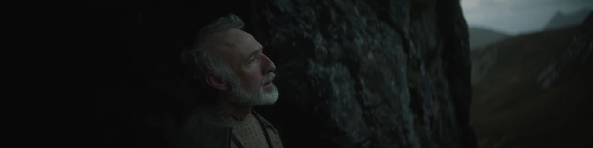 A man with a beard stands in a dim cave