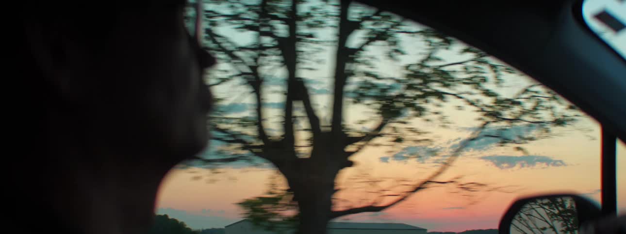 A man drives a car with trees water and the sky through the window