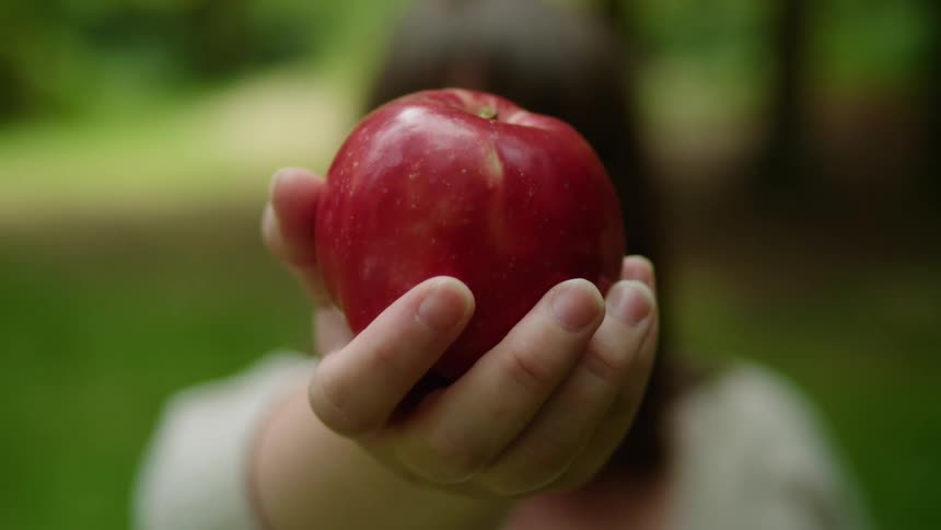 A person female stands outdoors and holds an apple in her hand which is the main focus of the shot