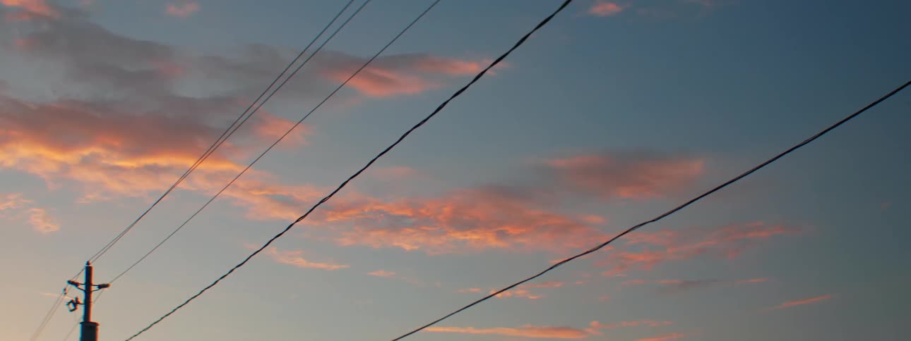 Clouds are tinted red in the sky near a utility pole