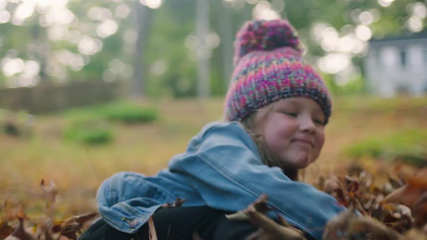 A girl playing in leaves in a yard outside
