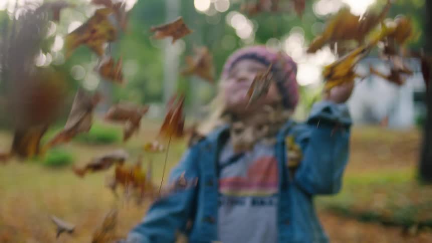 A young girl dressed in warm clothing grabs a pile of leaves which she throws over head