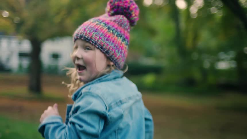 Little girl with a beanie and a denim jacket runs happily in the garden